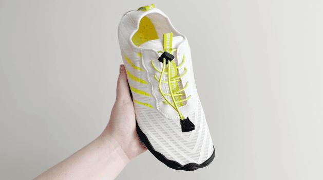 Lightweight white and neon green barefoot shoe held in one hand